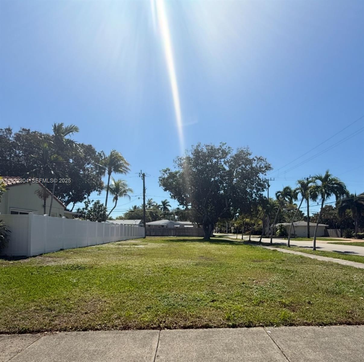 A vacant, grassy residential lot is bordered by a white fence and several palm trees — 1452 Jefferson St, Hollywood FL 33020, HOLLYWOOD, FL