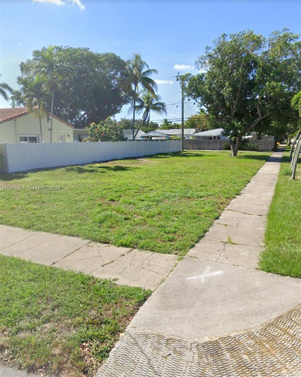 A vacant, grassy residential lot features a white vinyl fence and a concrete sidewalk — 1452 Jefferson St, Hollywood FL 33020, HOLLYWOOD, FL