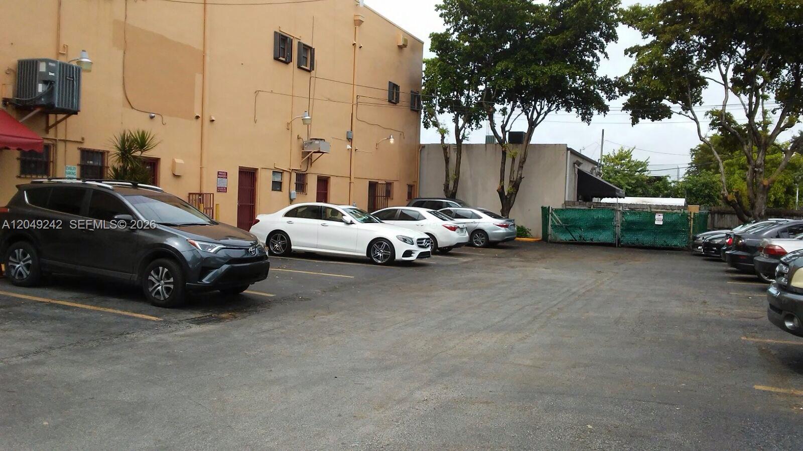 A parking lot sits in front of a tan commercial building with several parked cars — MIAMI, FL
