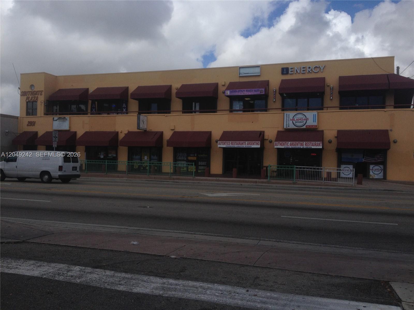 A two-story commercial building with red awnings and multiple storefronts sits along a street — MIAMI, FL