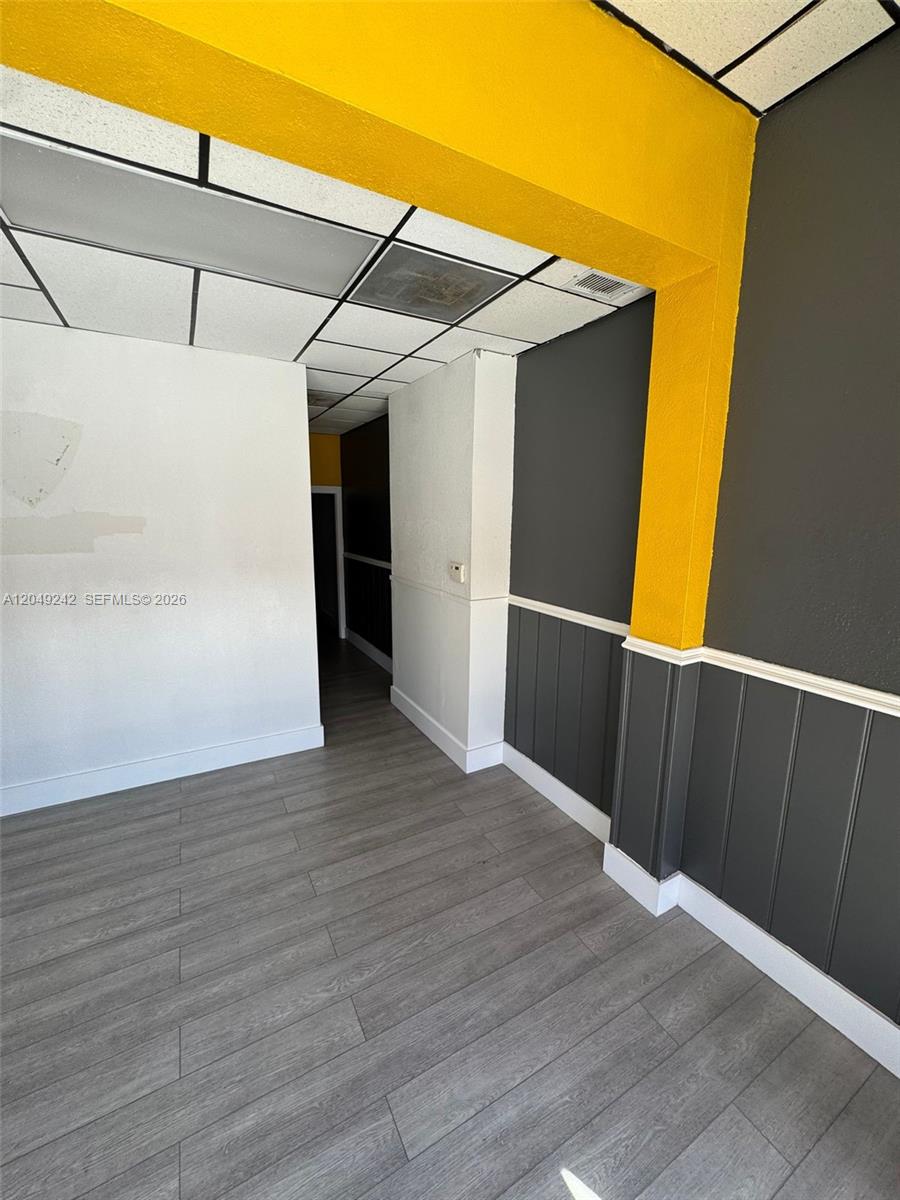 An interior room features gray wood-look flooring, white walls, and a yellow-painted structural beam — MIAMI, FL