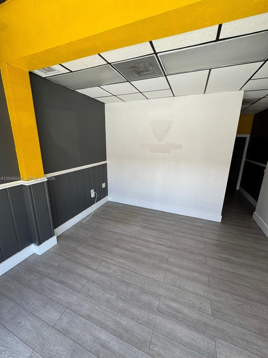 A room features gray wood-look flooring, dark gray wainscoting, a white wall, and yellow trim — MIAMI, FL