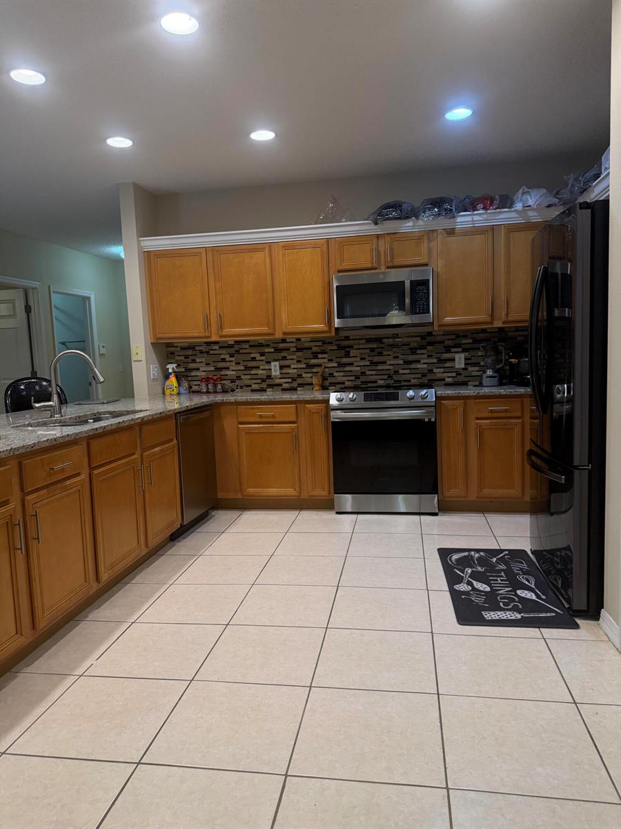 A kitchen featuring wood cabinets, granite countertops, stainless steel appliances, and a tiled floor — 133 Inconnu Court, FL 34759, FL