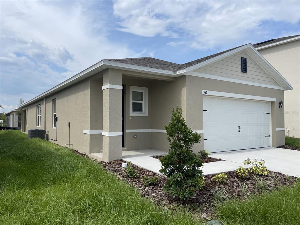 A single-story house with a tan stucco exterior, a white garage door, and a front porch — 927 WATERFALL BOULEVARD, DAVENPORT, FL