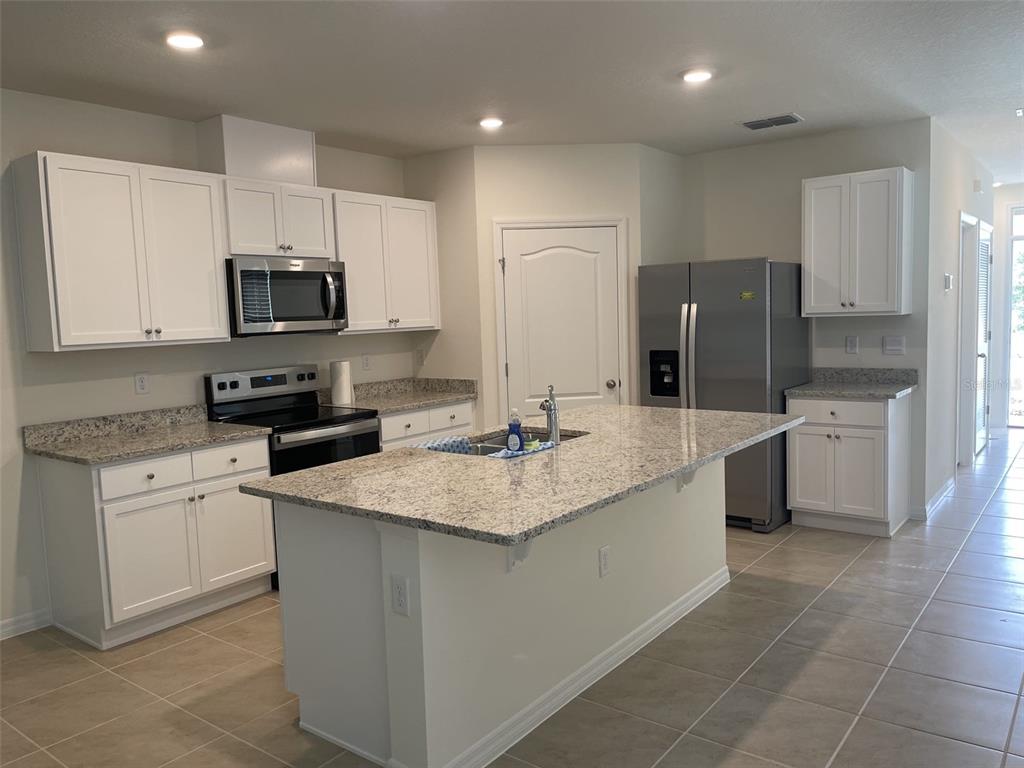 A kitchen features white cabinets, granite countertops, a center island, and stainless steel appliances — 927 WATERFALL BOULEVARD, DAVENPORT, FL