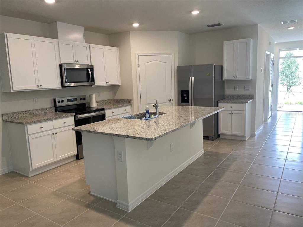 A kitchen features white cabinets, granite countertops, stainless steel appliances, and a central island — 927 WATERFALL BOULEVARD, DAVENPORT, FL