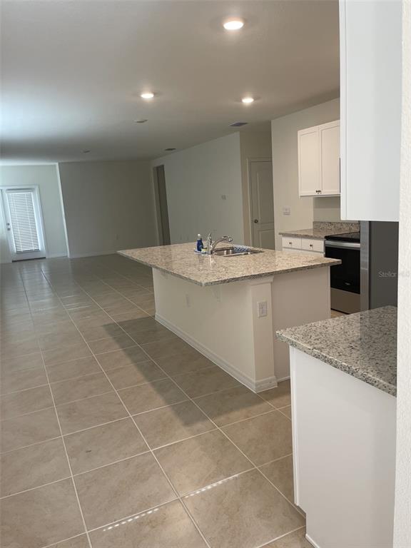 A kitchen with a granite-topped island and white cabinets opens into a tiled living area — 927 WATERFALL BOULEVARD, DAVENPORT, FL