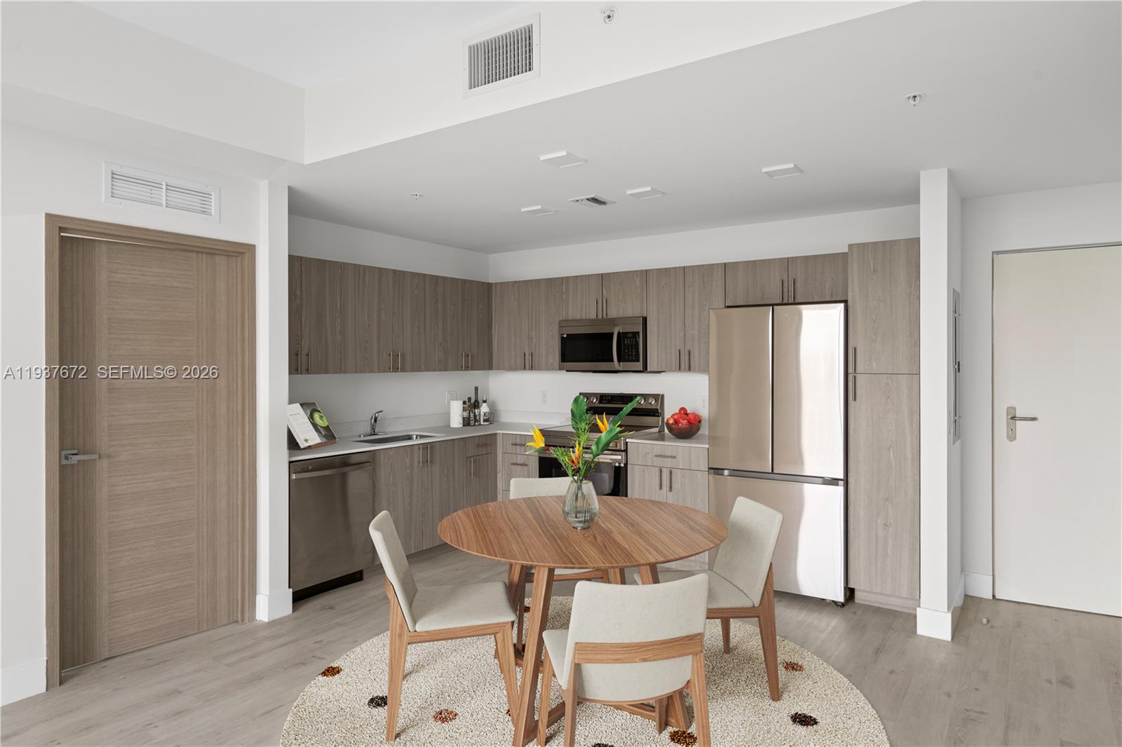 A modern kitchen features wood-grain cabinets, stainless steel appliances, and a round dining table — 1601 SW 32 Avenue # 313, Miami FL 33145, MIAMI, FL