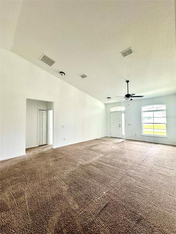 A spacious room with tan carpeting, a vaulted ceiling, a ceiling fan, and white walls — 102 AURELIA COURT, KISSIMMEE, FL