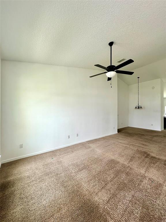 An empty room features beige carpeting, white walls, a ceiling fan, and a hanging light fixture — 102 AURELIA COURT, KISSIMMEE, FL