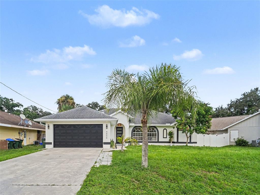 A single-story house with a dark garage door, a palm tree, and a concrete driveway — 4850 S SALFORD BLVD, NORTH PORT, FL