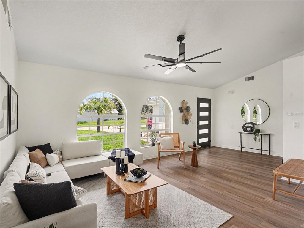 A bright living room features white walls, wood-look flooring, arched windows, and a modern ceiling fan — 4850 S SALFORD BLVD, NORTH PORT, FL