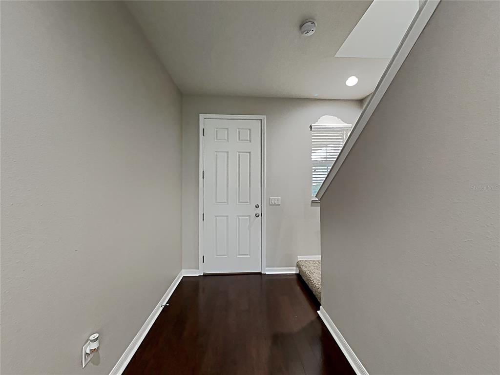 A hallway with dark wood flooring leads to a white door near a carpeted staircase — 7226 LUMBER PORT DRIVE, RUSKIN, FL