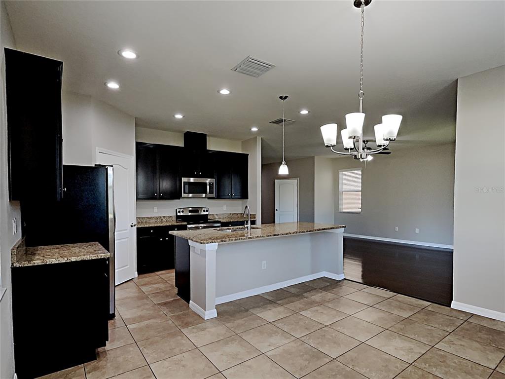 A kitchen features dark cabinets, granite countertops, a center island, and tile flooring — 7226 LUMBER PORT DRIVE, RUSKIN, FL