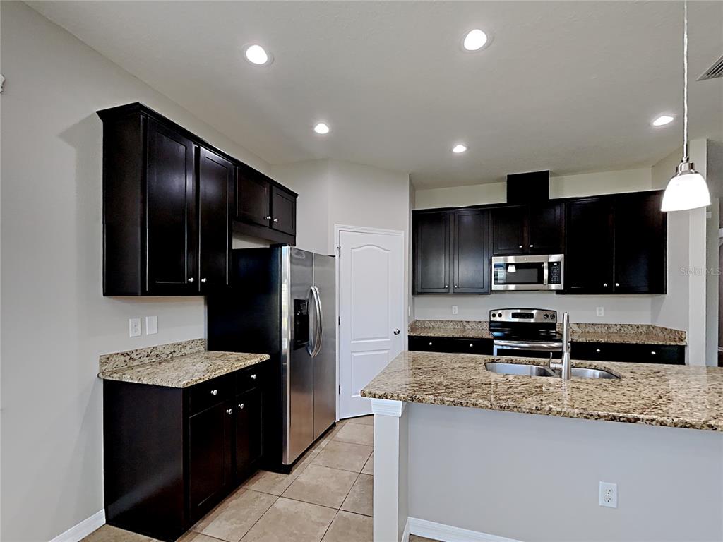 A kitchen features dark wood cabinets, granite countertops, stainless steel appliances, and tile flooring — 7226 LUMBER PORT DRIVE, RUSKIN, FL