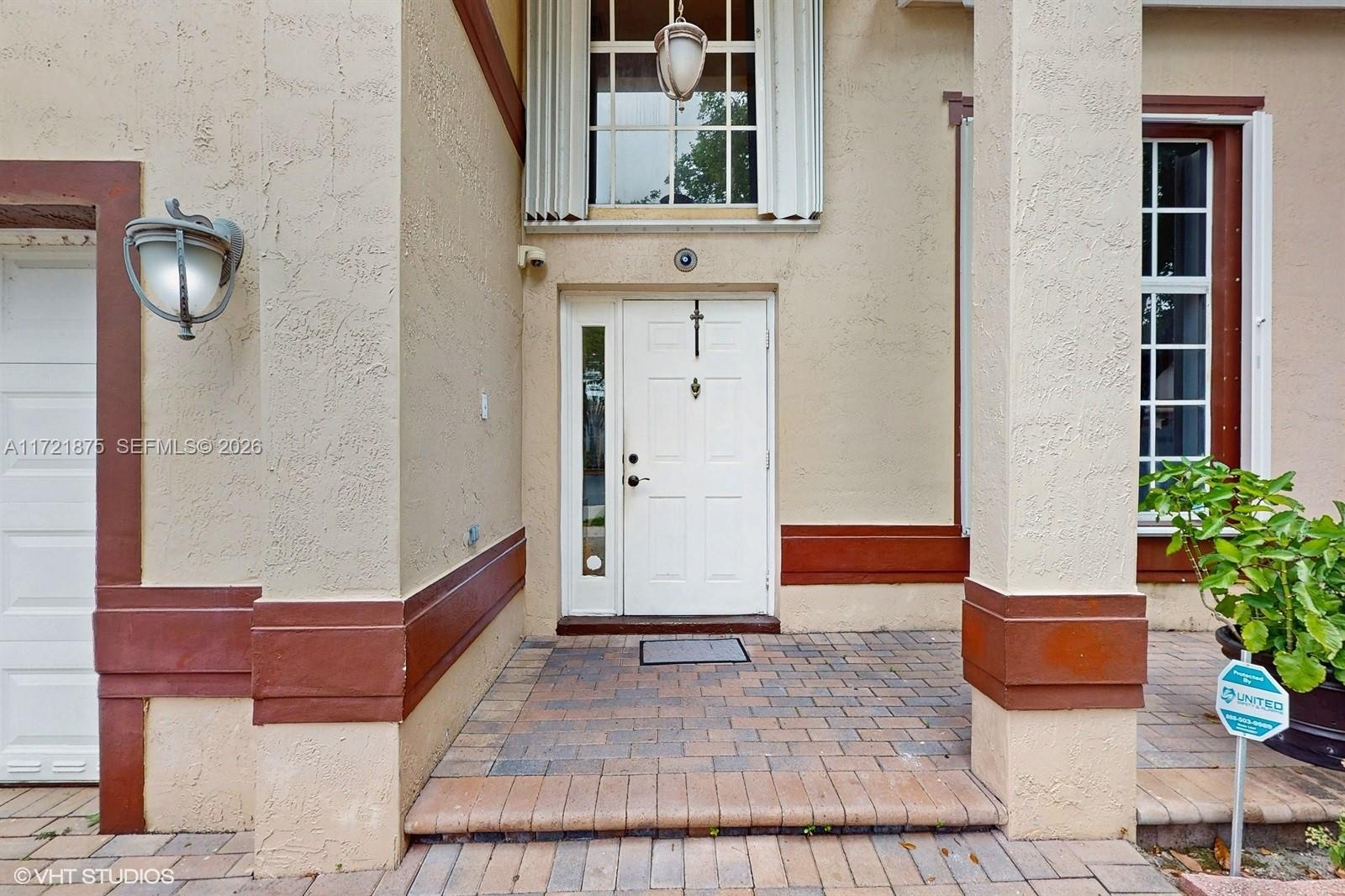 A white front door with a sidelight sits under a covered entryway with brick pavers — 5323 NW 109th Ct, Doral FL 33178, DORAL, FL