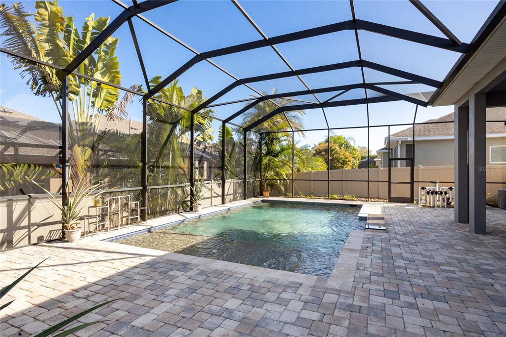 A screened-in patio features a rectangular swimming pool surrounded by light-colored stone pavers — 1308 CHARLEEN STREET, BRANDON, FL