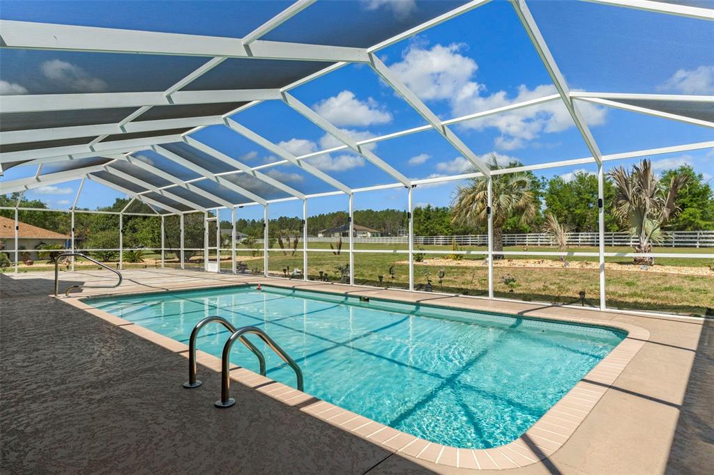 A rectangular swimming pool is enclosed by a white-framed screen cage on a concrete patio — 1231 E WHIRL AWAY CIRCLE, INVERNESS, FL