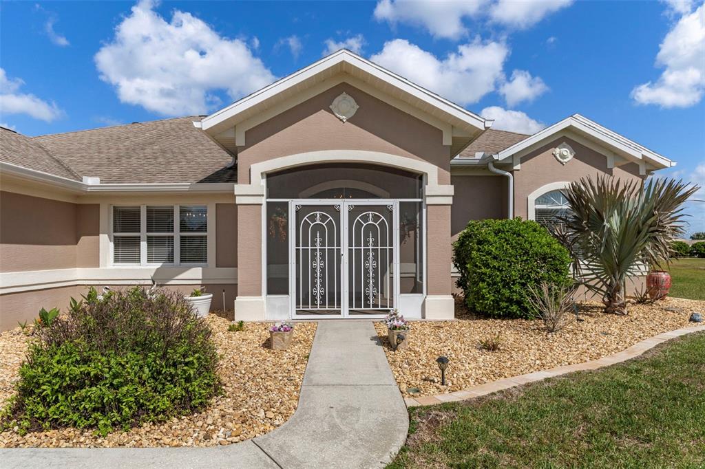 A tan house exterior features a screened front entryway, a concrete walkway, and gravel landscaping — 1231 E WHIRL AWAY CIRCLE, INVERNESS, FL