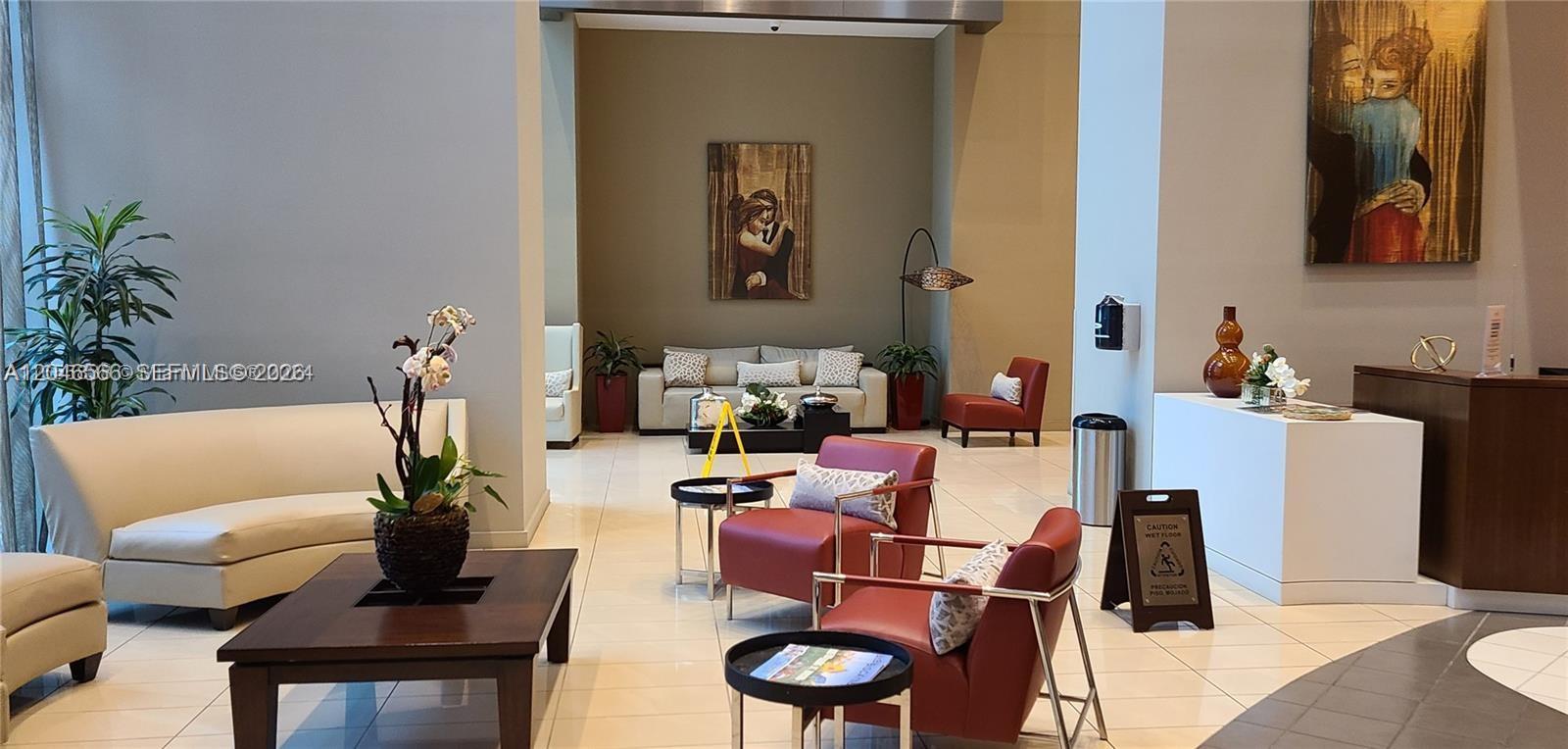 A modern lobby features white tile floors, red armchairs, a sofa, and abstract wall art — 300 S Biscayne Blvd # 2603, Miami FL 33131, MIAMI, FL