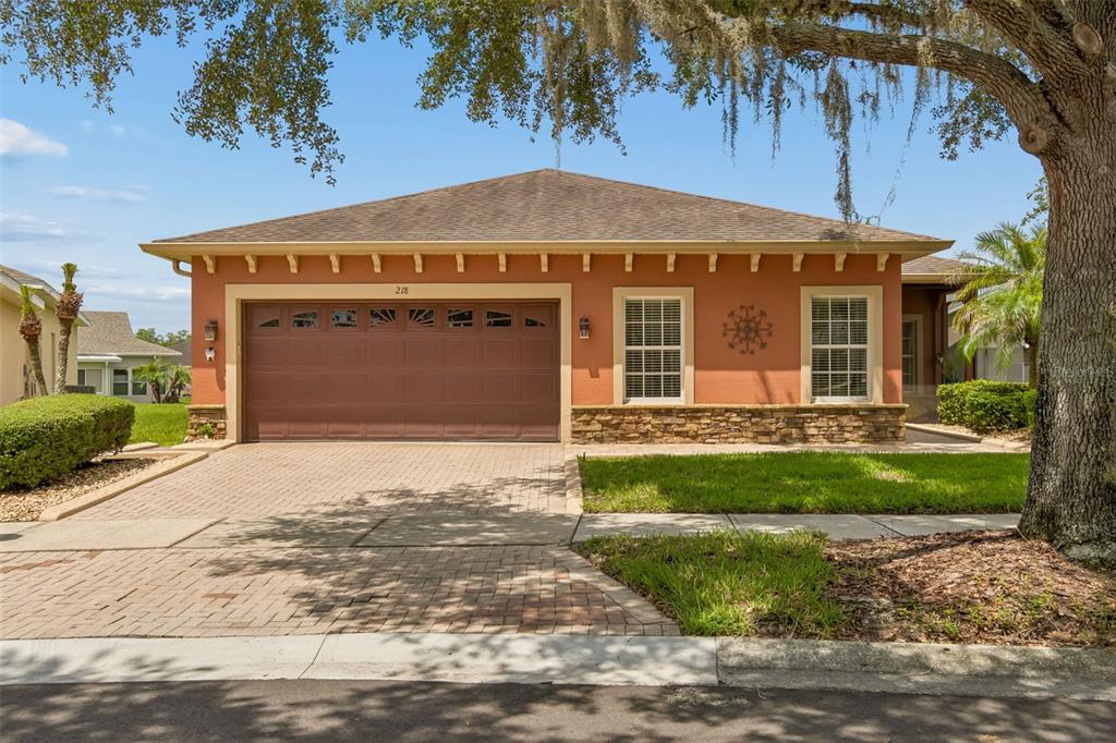 A single-story house with a terracotta-colored exterior, a two-car garage, and a paver driveway — 218 BAY DRIVE, KISSIMMEE, FL