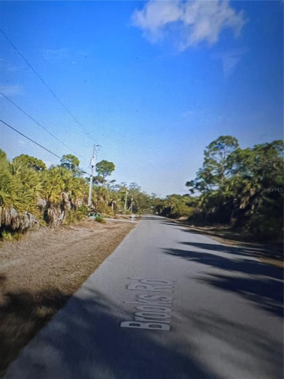 A paved road stretches into the distance, flanked by dense trees and power lines — 26319 BROOKS ROAD, PUNTA GORDA, FL