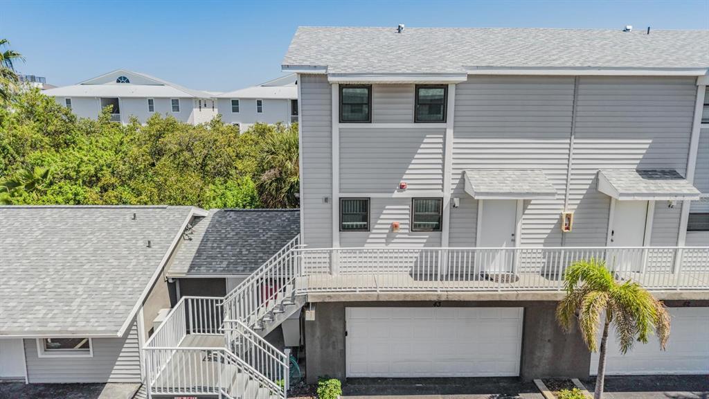 An exterior view of a two-story townhouse with a white garage, balcony, and metal staircase — 19823 GULF BOULEVARD UNIT 43, INDIAN SHORES, FL