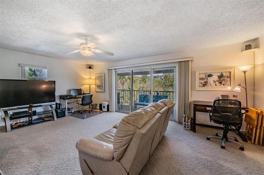 A living room features a beige sofa, two desks, a television, and a sliding glass door — 19823 GULF BOULEVARD UNIT 43, INDIAN SHORES, FL