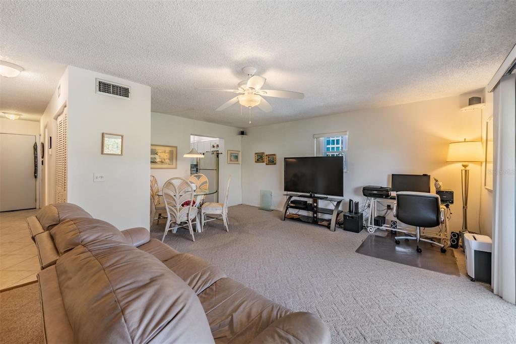 A living room with carpeted floors, a leather sofa, a dining area, and a desk — 19823 GULF BOULEVARD UNIT 43, INDIAN SHORES, FL