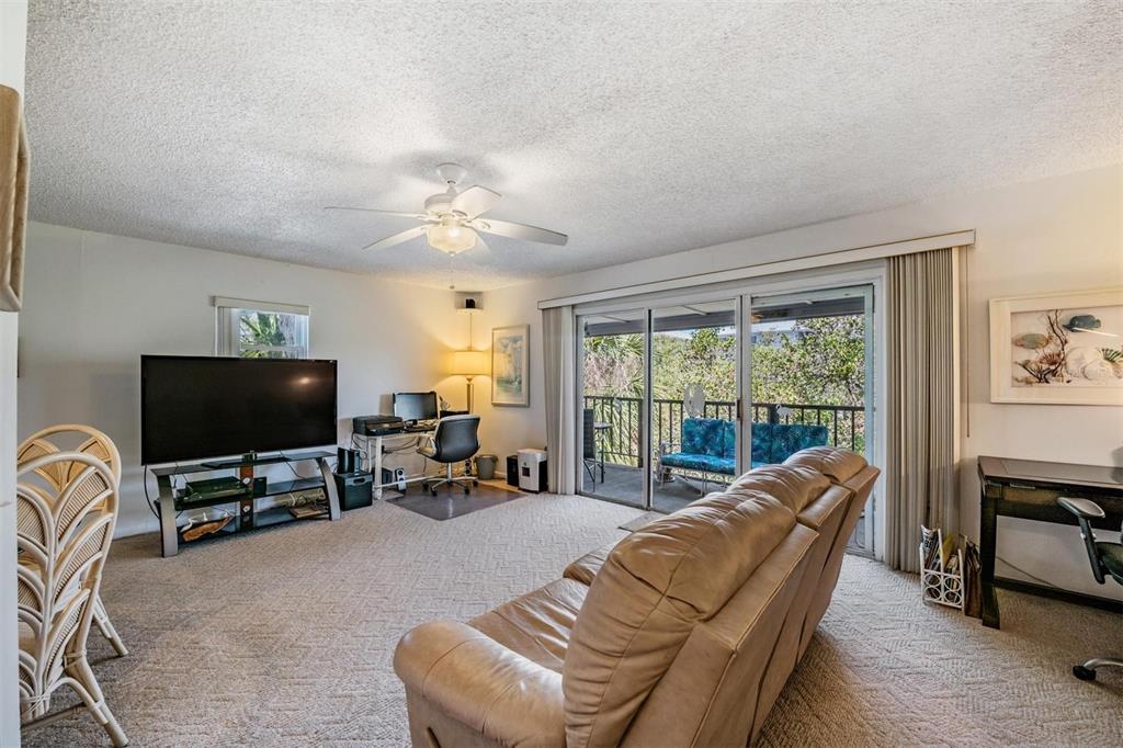 A living room features a beige sofa, television, desk, and sliding glass doors to a balcony — 19823 GULF BOULEVARD UNIT 43, INDIAN SHORES, FL