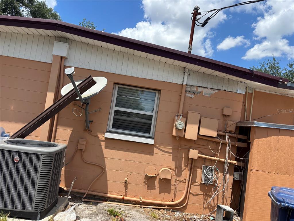 The exterior of a peach-colored concrete block house features an HVAC unit and utility boxes — 1320 LARSEN LN, TAMPA, FL