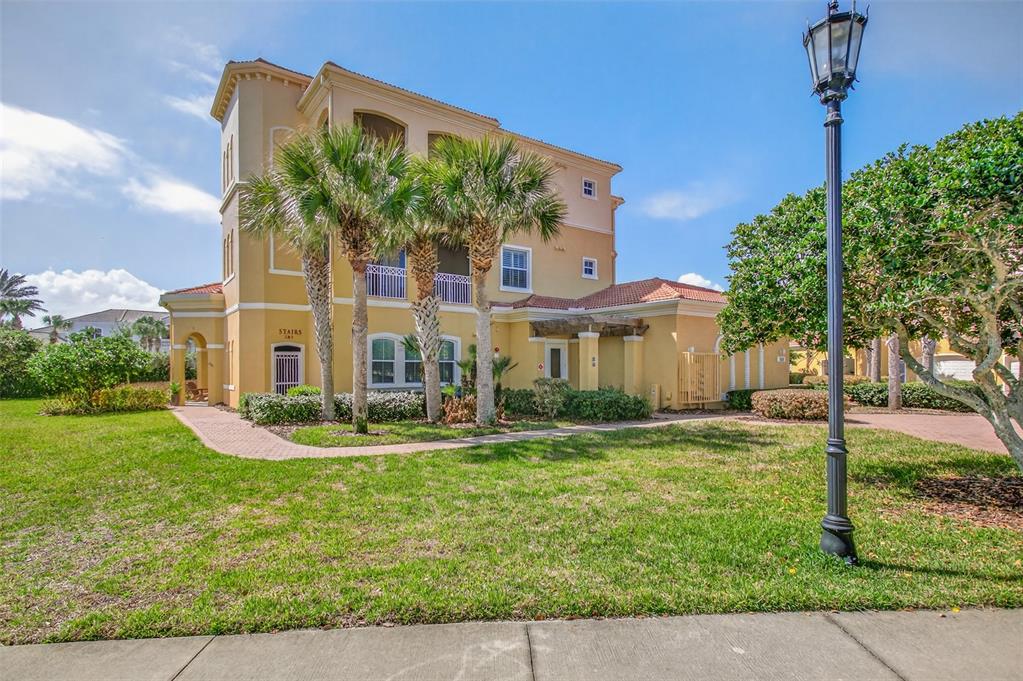 A three-story tan stucco building with palm trees and a lamp post on the lawn — 160 AVENUE DE LA MER UNIT 1903, PALM COAST, FL