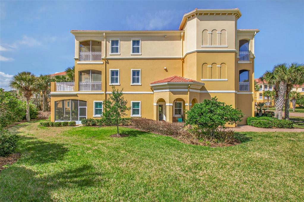 A three-story yellow stucco building with screened balconies and a landscaped lawn — 160 AVENUE DE LA MER UNIT 1903, PALM COAST, FL