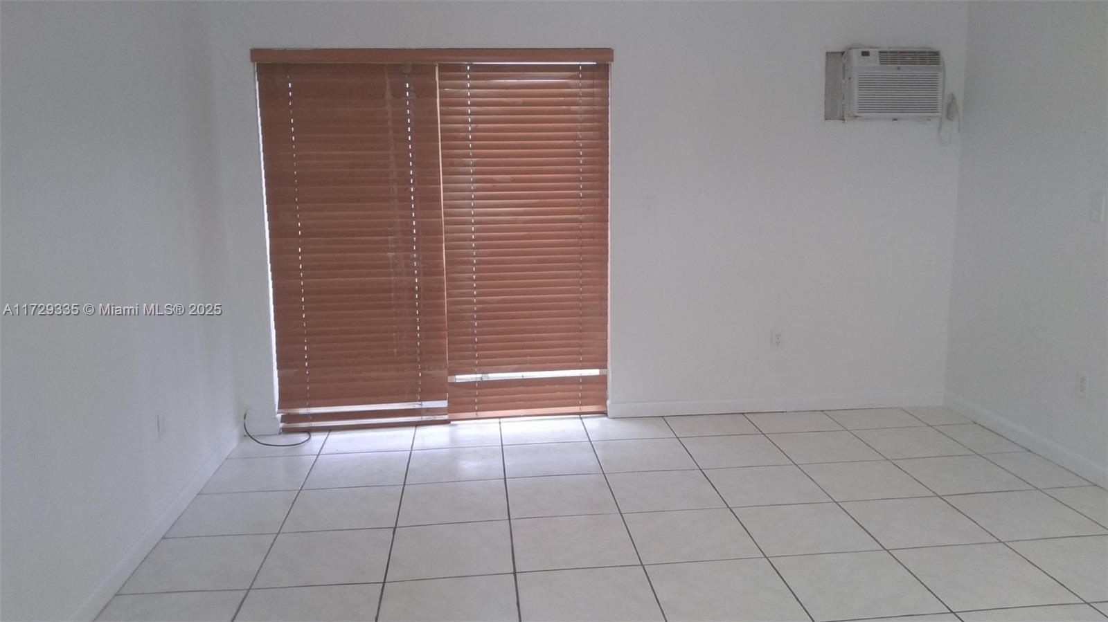 An empty room features white walls, light-colored tile flooring, wood blinds, and a wall-mounted air conditioner — 1441 Lincoln Rd # 414, Miami Beach FL 33139, MIAMI BEACH, FL