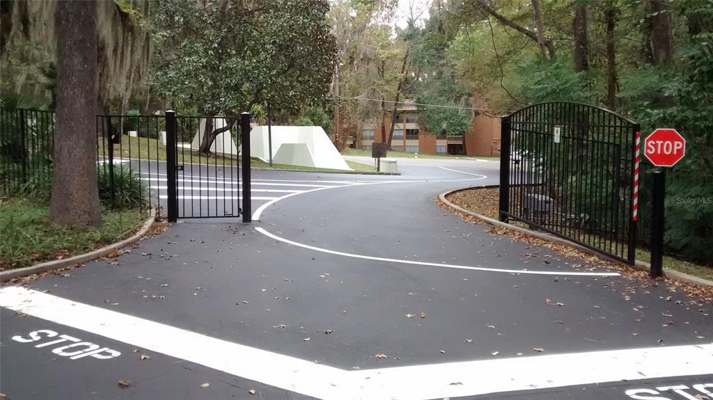 An open black metal gate leads to a paved driveway with stop signs and markings — 1719 NW 23RD AVENUE UNIT 5A, GAINESVILLE, FL