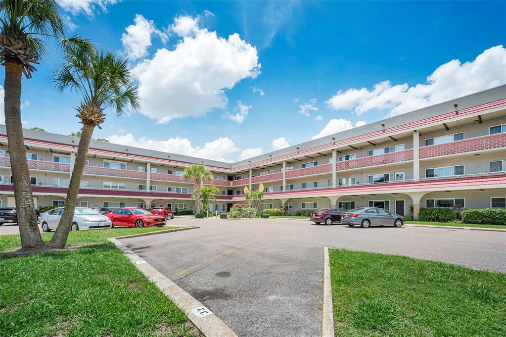 A three-story apartment building with a parking lot and palm trees under a blue sky — 2072 AUSTRALIA WAY W UNIT 32, CLEARWATER, FL