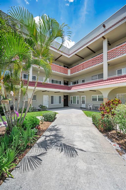 A concrete walkway leads to the entrance of a multi-story apartment building with palm trees — 2072 AUSTRALIA WAY W UNIT 32, CLEARWATER, FL