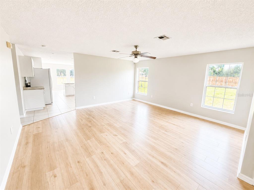 An open living room with light wood flooring, a ceiling fan, and a kitchen view — 5910 BAKER ROAD, NEW PORT RICHEY, FL