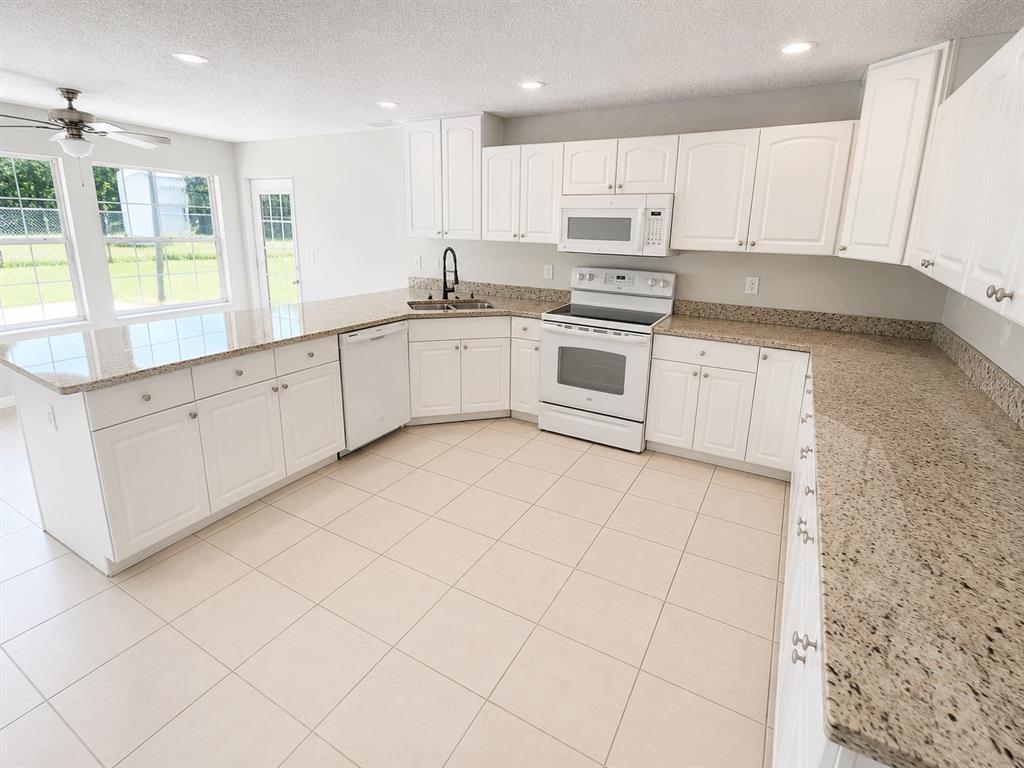 A kitchen features white cabinets, granite countertops, tile flooring, and white appliances — 5910 BAKER ROAD, NEW PORT RICHEY, FL
