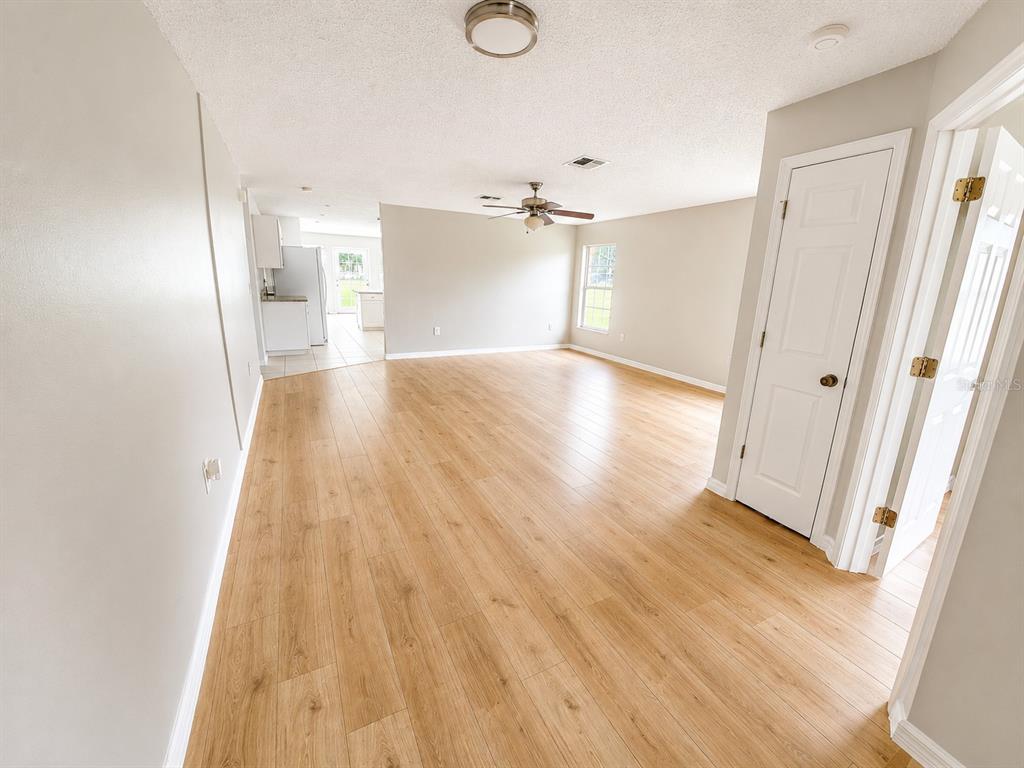 An open-concept living area features light wood-look flooring, neutral walls, and a ceiling fan — 5910 BAKER ROAD, NEW PORT RICHEY, FL