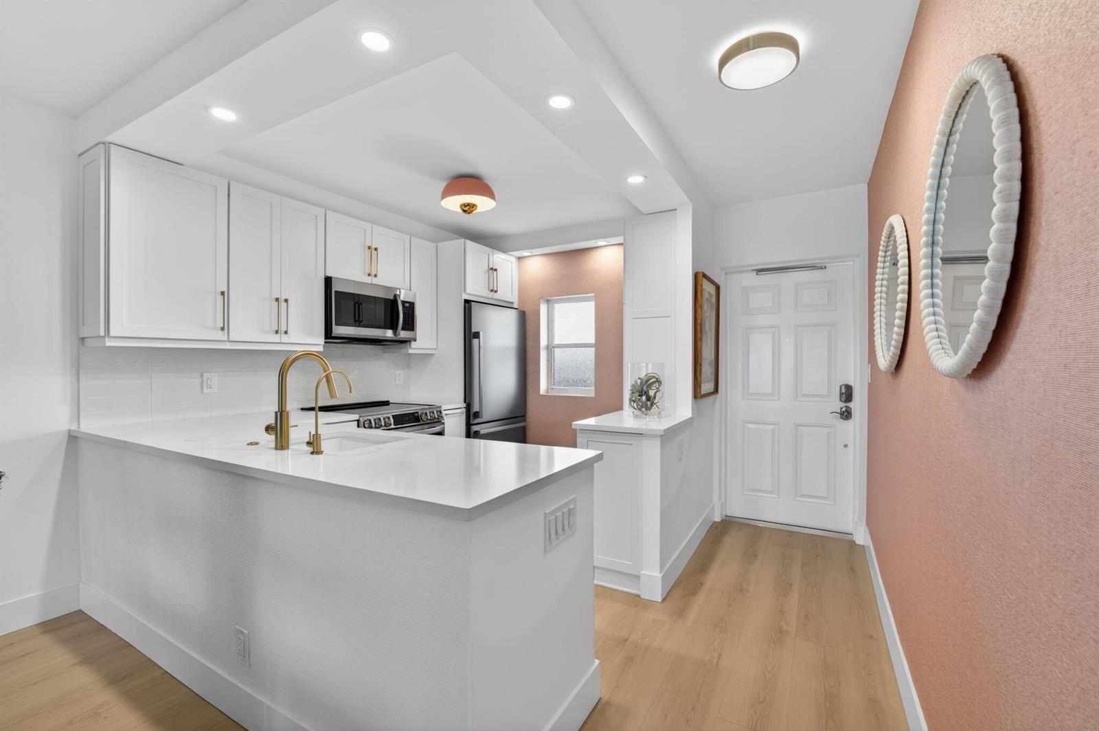 A kitchen with white cabinets, gold hardware, a peninsula, and a pink accent wall — 1427 E Hillsboro Boulevard # 628, Deerfield Beach FL 33441, DEERFIELD BEACH, FL