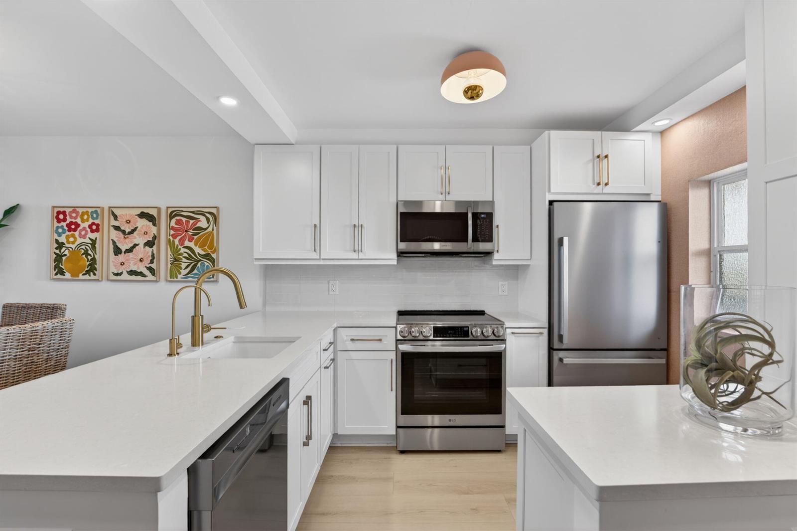 A modern kitchen features white cabinets, stainless steel appliances, gold hardware, and white quartz countertops — 1427 E Hillsboro Boulevard # 628, Deerfield Beach FL 33441, DEERFIELD BEACH, FL