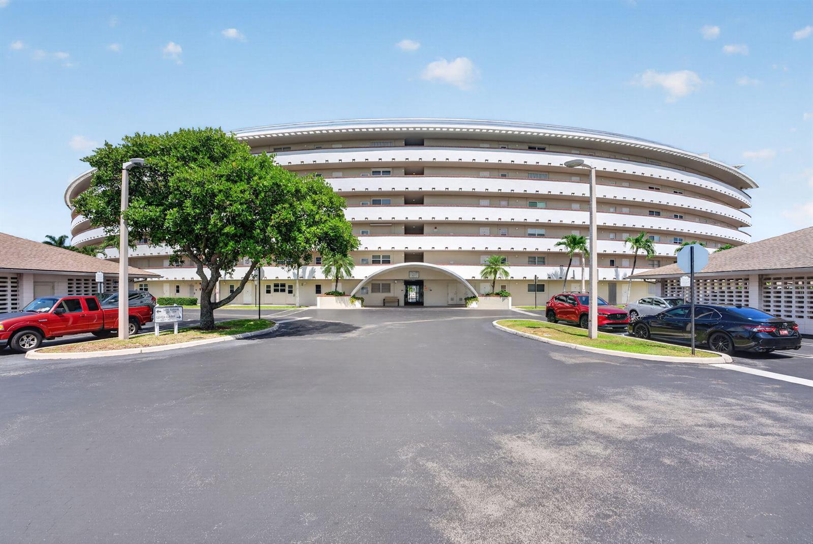 A large, circular multi-story residential building stands behind a paved parking lot with trees — 1427 E Hillsboro Boulevard # 628, Deerfield Beach FL 33441, DEERFIELD BEACH, FL
