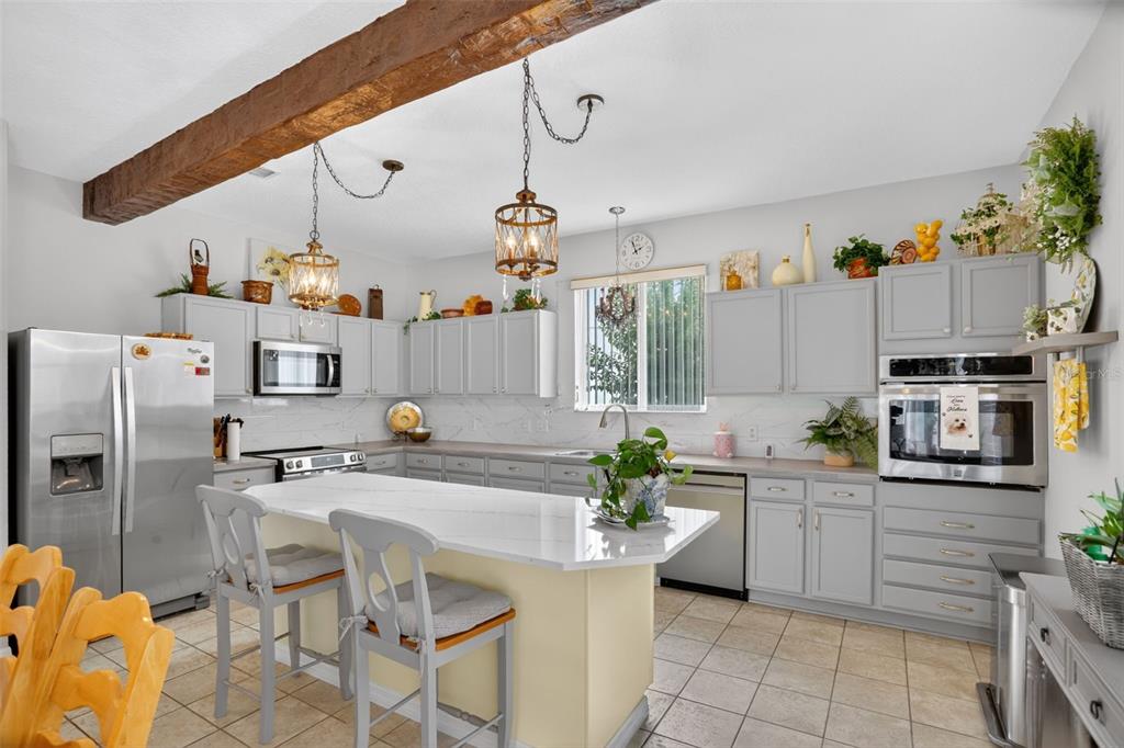 A kitchen features grey cabinets, a white island, stainless steel appliances, and a wooden ceiling beam — 388 SAND RIDGE DRIVE, DAVENPORT, FL
