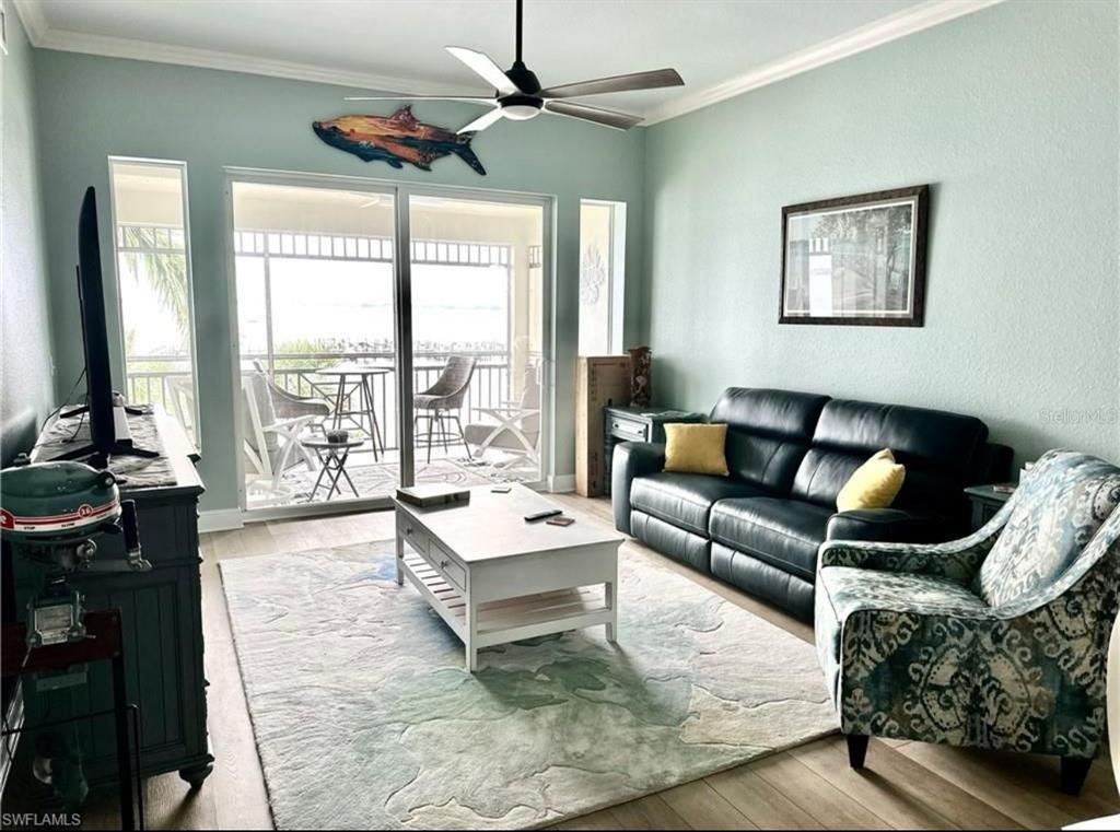 A living room features a black leather sofa, patterned armchair, coffee table, and ceiling fan — 5114 MELBOURNE STREET UNIT A302, PUNTA GORDA, FL