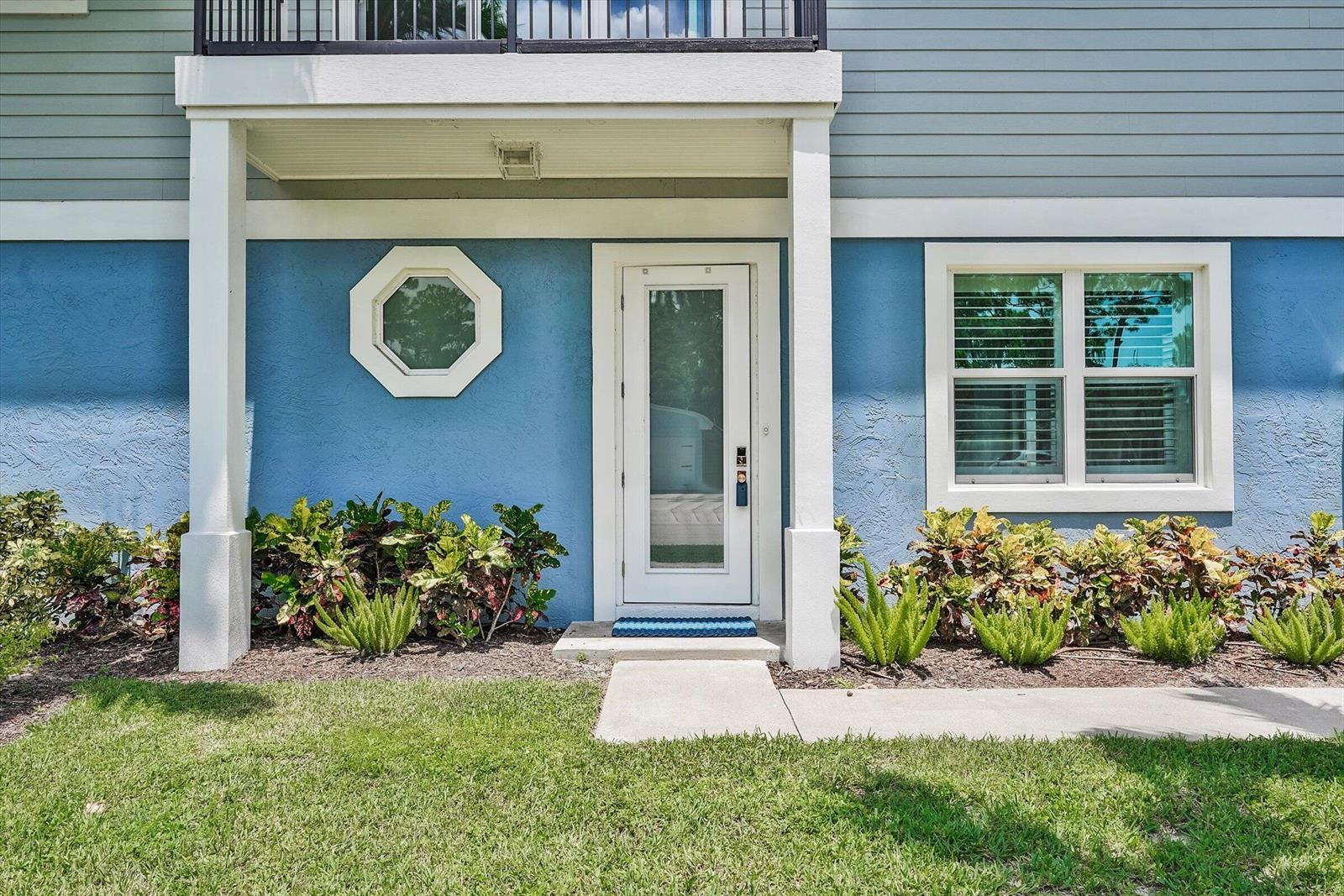 A blue exterior wall features a white front door, an octagonal window, and landscaping — 425 Hugh Street, Jupiter FL 33458, JUPITER, FL