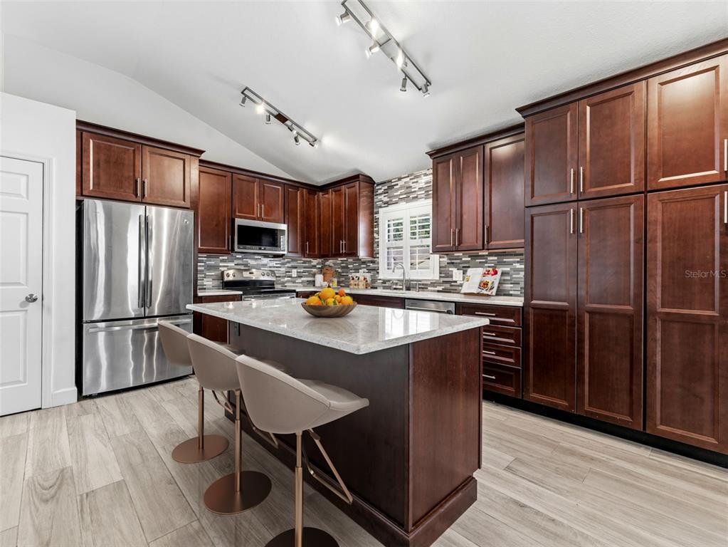 A kitchen features dark wood cabinets, a central island with bar stools, and stainless appliances — 13419 EUDORA PLACE, TAMPA, FL