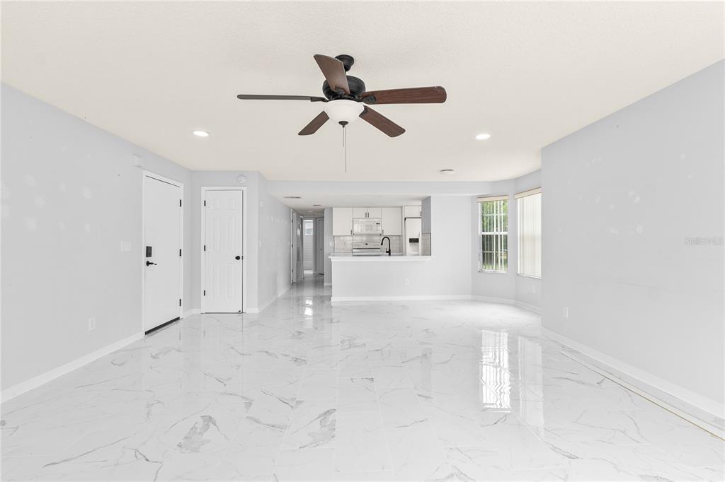 An open-concept living area features white marble-look tile flooring and a kitchen in the background — 2036 ROYAL BAY BOULEVARD UNIT 59, KISSIMMEE, FL