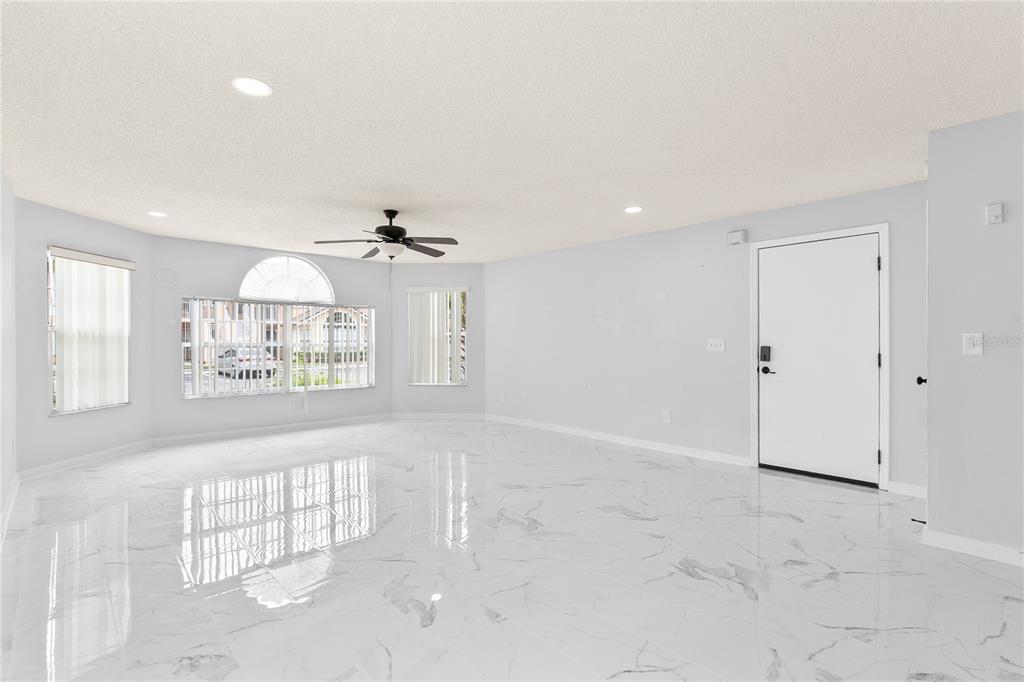 A bright, empty living room features white marble-look tile flooring and a ceiling fan — 2036 ROYAL BAY BOULEVARD UNIT 59, KISSIMMEE, FL