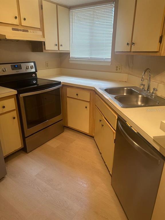 A kitchen features light-colored cabinets, a stainless steel stove, a double sink, and vinyl flooring — 1940 LAKE ATRIUMS CIRCLE UNIT 93, ORLANDO, FL